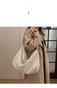 Detail view of a large white canvas hobo bag with brown polka dots on a model