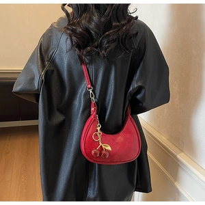 Detailed view of red crescent shoulder bag with a decorative cherry pendant charm