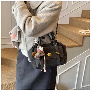 Detail shot of a charcoal messenger bag with golden twist lock and plush bear charm