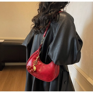 Detail of red crescent shoulder bag featuring a gold cherry charm and glossy PU leather