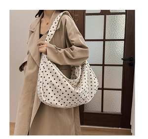 Detailed side view of a beige canvas tote bag with brown polka dots on a model