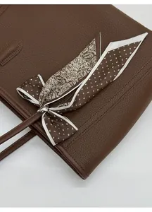 Detail of dark brown leather tote bag with lychee texture and silk scarf decoration
