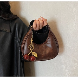 Detail of dark brown faux leather hobo bag featuring a cherry pendant and litchi texture