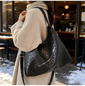Detail of black woven leather shoulder bag with diagonal zipper in a winter street setting