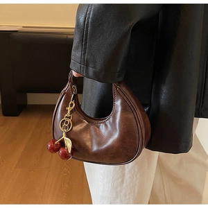 Detail of dark brown hobo crescent bag with red cherry charm held by model