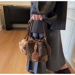 Detail of leopard print bucket bag with brown leather accents and plush bear charm
