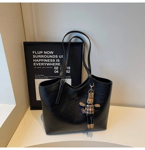 Detail of black leather tote bag with silver buckle strap and bunny plush pendant accessory