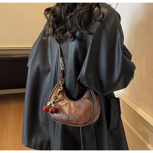 Detail of a vintage brown crescent bag with a decorative red cherry pendant charm
