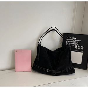Macro detail of black suede tote bag with decorative buckle strap on white marble surface