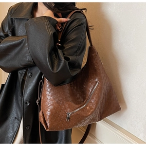 Detail of dark brown woven leather tote with silver zipper worn by a model in a leather coat