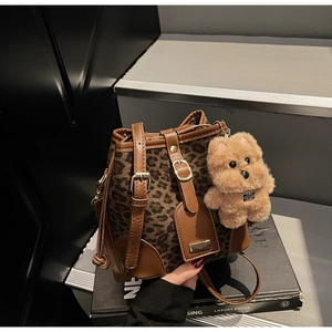 Detail view of leopard print bucket bag featuring brown leather trim and plush dog charm