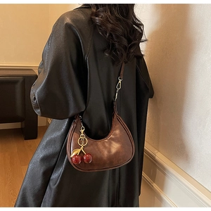 Detail of dark brown leather crescent bag with a decorative red cherry pendant