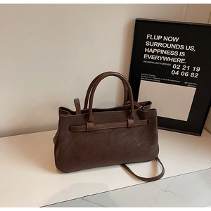 Detail of dark brown matte leather tote bag featuring buckle strap and crossbody strap