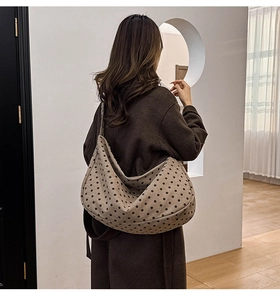 Detailed back view of a large polka dot hobo bag worn with a long brown coat