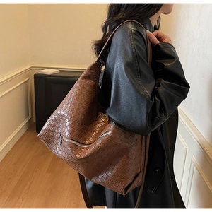 Brown woven leather tote bag with side zipper detail worn over the shoulder by model