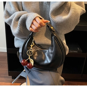 Close-up of black crescent shoulder bag with a glittery red cherry charm accessory