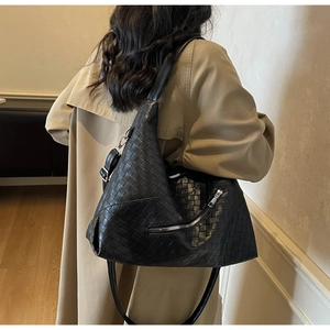 Close-up of black woven shoulder bag featuring textured weave and decorative zipper pocket