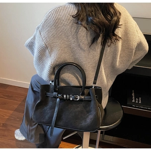 Detail of black matte leather tote bag featuring a decorative buckle and versatile straps