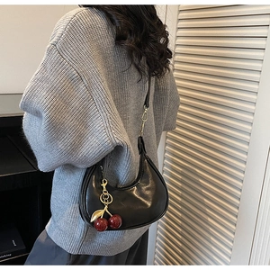 Detail of a black crescent shoulder bag with a red cherry pendant and gold hardware accents