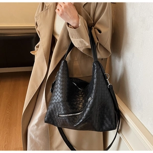 Close-up of black woven leather tote bag with silver zipper detail on model in trench coat