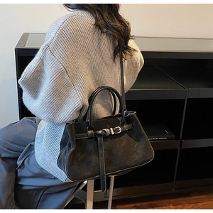 Detail of black suede tote bag with silver metal buckle on a grey knit sweater