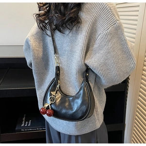 Detail of black glossy leather hobo bag with red cherry charm and golden hardware