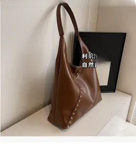 Detail of brown litchi leather tote bag featuring curved silver rivet studs on the side