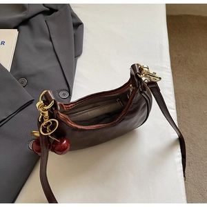 Detail of dark brown crescent bag with polished finish and a red cherry charm