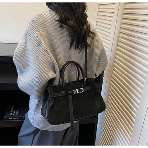 Detail view of black matte leather tote bag with silver buckle on a grey sweater