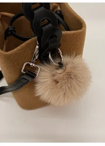 Close-up of brown wool felt bucket bag with soft plush ball charm and black leather strap