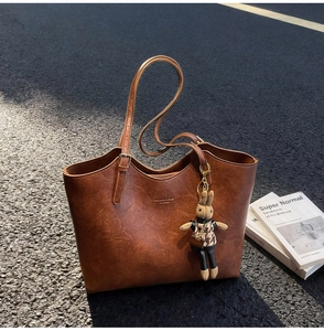 Detail of vintage brown tote bag with leather texture and rabbit charm on asphalt