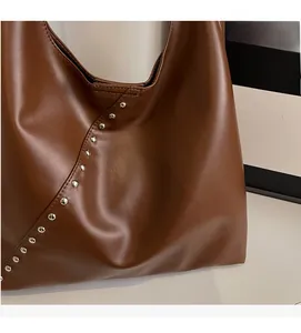 Detailed view of dark brown tote bag with silver metal studs and smooth leather texture