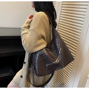 Detail of dark brown woven shoulder bag worn by model in a cozy indoor setting
