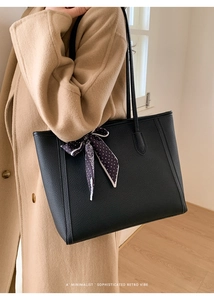 Detail of black leather tote bag with polka dot scarf on handle worn with khaki coat