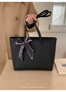 Detail of black pebbled leather tote bag with a geometric pattern scarf on handle