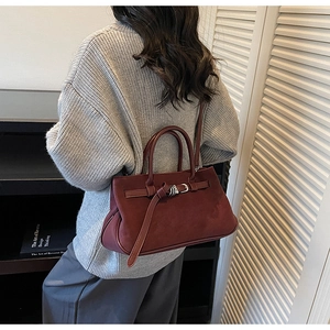 Detail view of burgundy matte tote bag with buckle accessory on vintage bookshelf background
