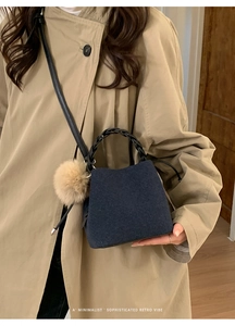 Detail of navy felt bucket bag with black woven handle and soft fur ball charm
