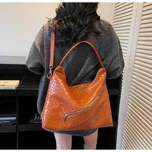 Detail of orange-brown woven leather tote bag with diagonal zipper and adjustable strap