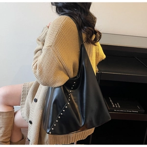 Side view of large black hobo shoulder bag with silver stud accents on a model