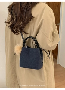 Detail of blue denim bucket bag with woven handle and fluffy keychain on trench coat