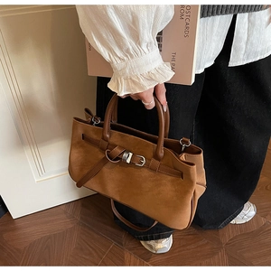 Top view of brown suede tote bag with metal buckle and shoulder strap in a stylish room
