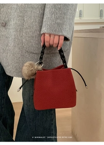 Close-up of deep red woven bucket bag with twisted rope handle and plush charm detail