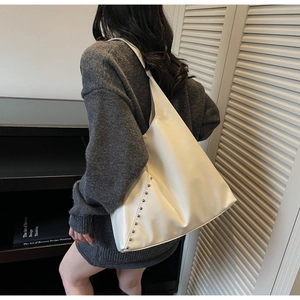 Detailed view of cream-white oversized tote bag featuring silver studs on soft leather