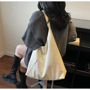 Chic beige shoulder bag with silver stud accents styled in a cozy library setting