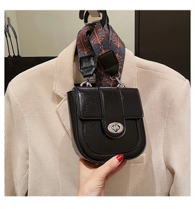 Détail du sac noir brillant avec fermoir argenté ovale et poignée ornée d'un foulard en soie