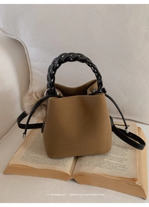 Detail of wool bucket bag with woven handle and plush pompom charm on book