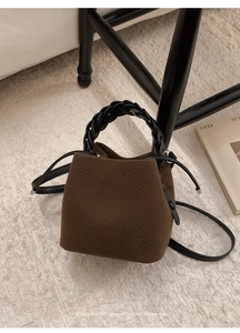 Detail view of brown textured fabric bucket bag with black woven handle on plush rug