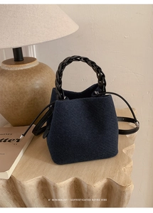 Detail of navy wool bucket bag with black woven handle and minimalist leather strap