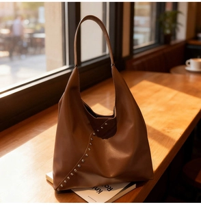 Detailed view of brown leather hobo bag with silver studs on a wooden table