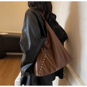 Detail of large brown leather tote bag featuring stylish silver rivets and wide shoulder strap